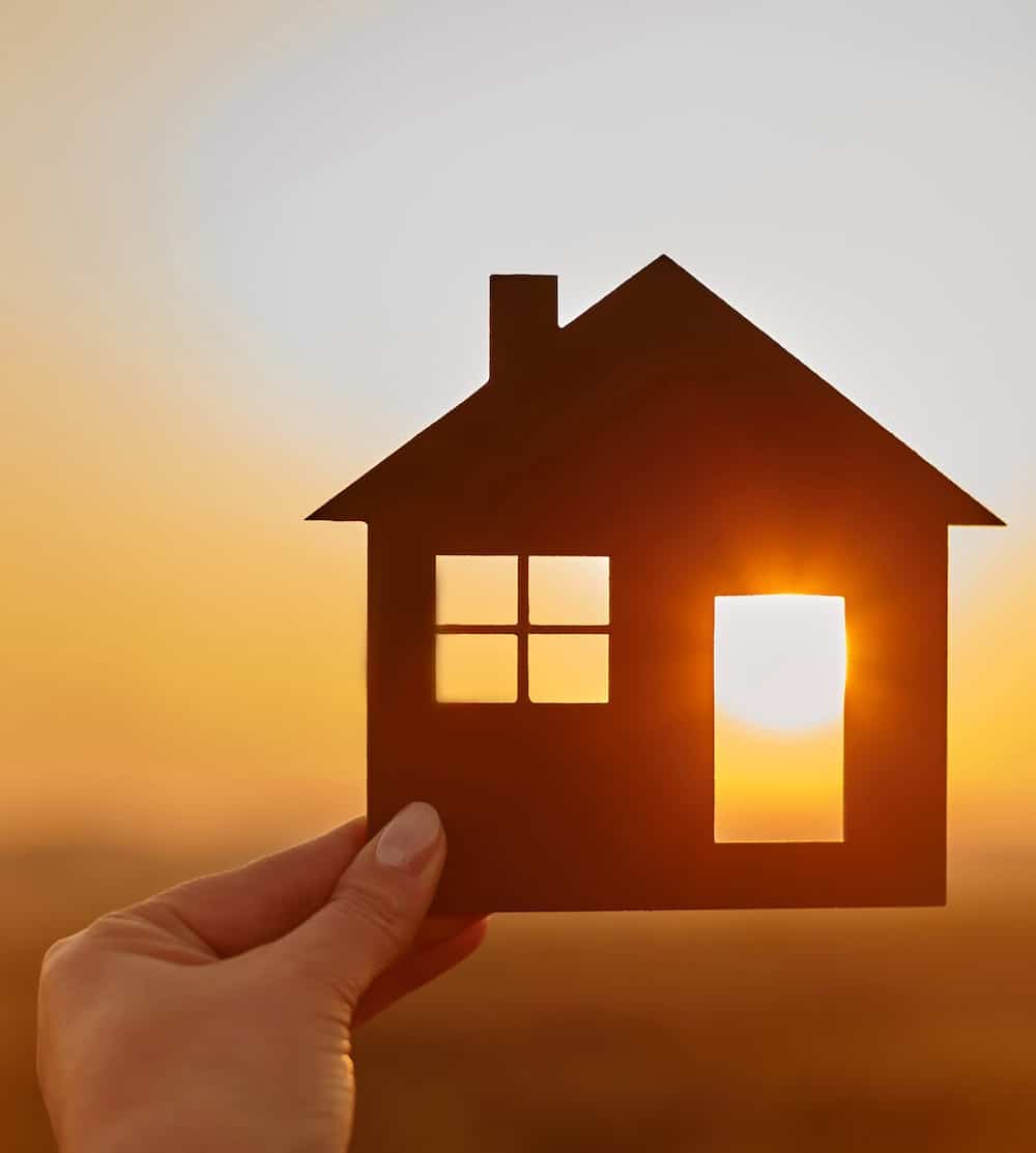 Woman hand holds wooden house against the sun