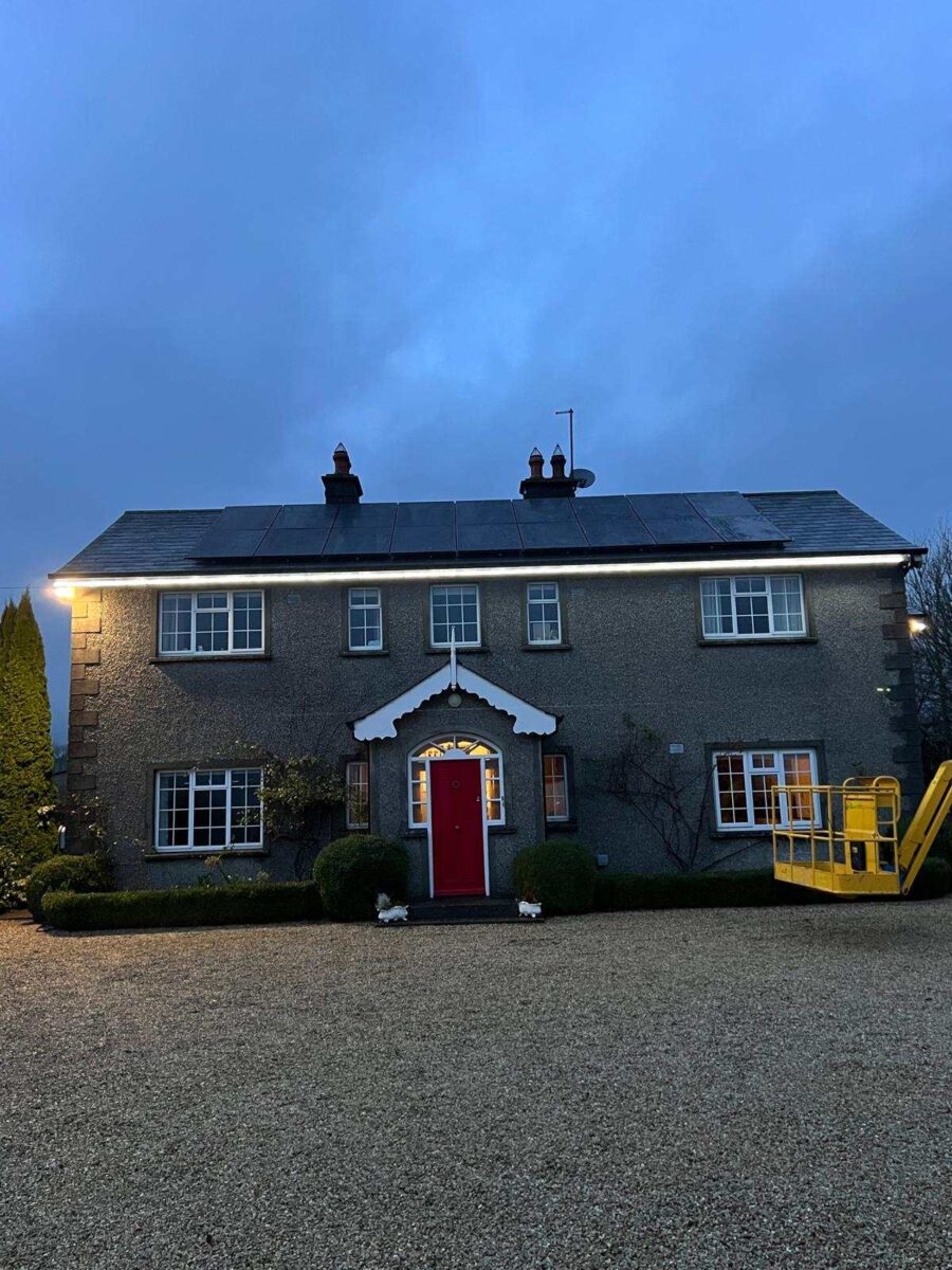 Charming grey house with a red door, illuminated by roofline lights.